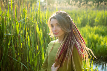 Fototapeta premium Dreadlocks woman wearing green shirt in a city park during a sunset, be free, boho, hippy lifestyle concepts