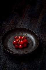 dark red and fresh cherries in a black ceramic bowl on wooden background with selective focus