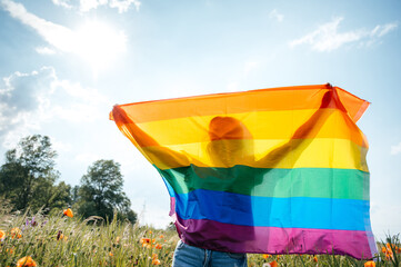 Girl stands on the poppy field in the nature and covering her face with the flag of LGBT, the...