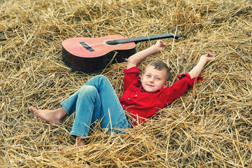 Portrait of a boy with an acoustic guitar in a field near a haystack