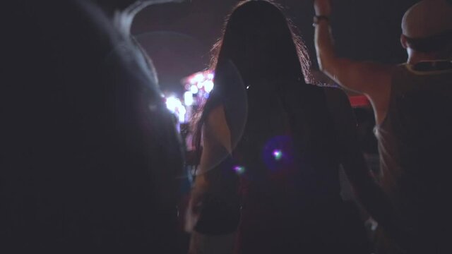 Night time music festival. A woman dances in a psychedelic trance to the live concert at night. Lights flash and glare bright colors through the crowd of people.