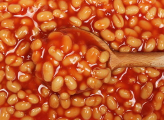 Cooked white beans in red tomato sauce surface with wooden spoon background and texture