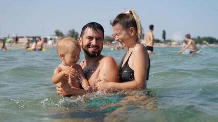 Fototapeta na wymiar Young family standing in water in sea. Father holding little son in arms