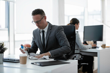 Handsome businessman disinfecting desk in the office.	