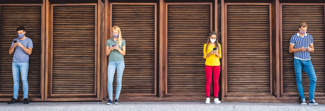 Young people wearing face mask using mobile phone keeping social distance - Millennial friends watching new media trends on smartphones during corona virus outbreak - Youth and technology concept