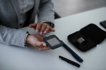 Close up of businesswoman using digital glucometer in office. Young woman checking blood sugar level	