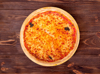 Whole delicious pizza with mozzarella, bocconcini and basil leaves or pizza margherita on a round wood plate which is on the wooden rustic table, top view