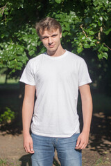 a happy young man stands in the sun in a white t shirt with a smile on his face