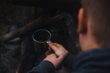 Fototapeta na wymiar Metal camping mug with coffee in a man's hand. Adventure, travel, tourism and camping concept.