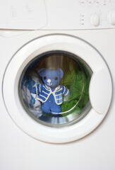 Clothes and teddy bear toy behind the window of the washing machine