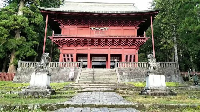 Moving towards the red entrance gate of Iwakiyama Shrine with two stone statues in front of it