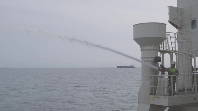 professional mechanic in protective helmet checks fire hydrant jet aboard Natig Aliev oil tanker against sea and grey sky