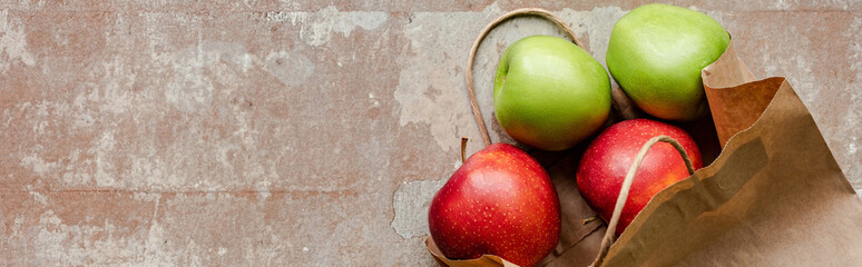 top view of paper bag with red and green apples on weathered beige surface, panoramic crop