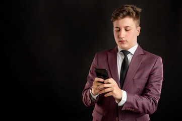 Law student with blond hair dressed in burgundy jacket, white shirt and black tie reading and sending text messages on cellphones