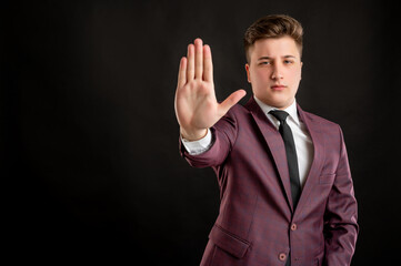 Law student with blond hair dressed in burgundy jacket, white shirt and black tie showing stop sign