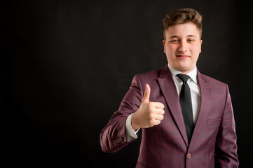 Law student with blond hair dressed in burgundy jacket, white shirt and black tie showing thumbs up