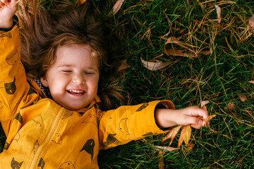 Adorable little girl 3-4 years old lying on the grass on an autumn day. Cute girl-toddler resting and having fun in the Park. The child smiles close-up and looks at the camera. The view from the top.