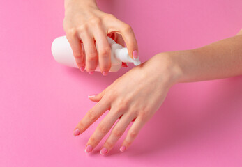 Female hand holding skincare product bottle on pink