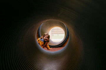 A little girl climbs in the pipes. Modern and safe children's Playground. Round and long tunnel. Overcome obstacles. Children's curiosity and discovery of everything new.