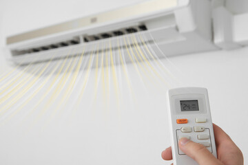 Man operating air conditioner with remote control indoors, closeup