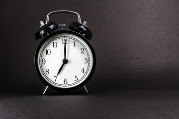 An old alarm clock showing 7 o'clock on a black background
