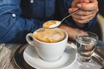 Cappuccino, woman drinking coffee at cafe. Close-up view at spoon and cup 