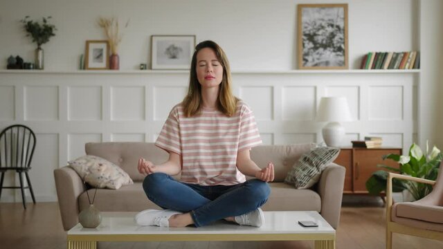 young woman sits alone on coffee table in lotus pose with aromatherapy. meditates with closed eyes. relaxes to get rid of stress, and have refresh break. phone call irritates and makes angry