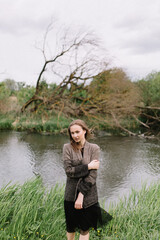 Girl model portrait near the river with hair. Pensive look. Beautiful eyes. Stylish clothes on the nature. Trees and plants.