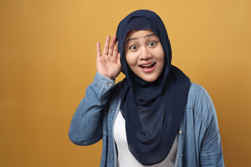 Asian muslim woman wearing hijab smiling while doing hearing gesture, shocked surprised expression to hear gossip