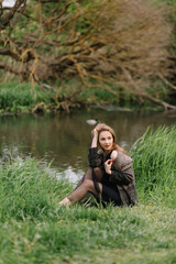 Stylish model girl in clothes on the grass near the small river reeds trees