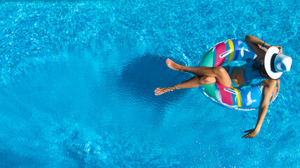 Beautiful girl in hat in swimming pool aerial top view from above, young woman relaxes and swims on inflatable ring donut and has fun in water on family vacation, tropical holiday resort
