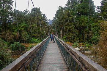 Couple over the bridge on the track on the way to Lake Matheson. New Zealand South Island. June ‎12, ‎2018