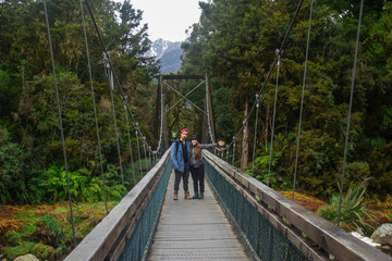 Couple over the bridge on the track on the way to Lake Matheson. New Zealand South Island. June ‎12, ‎2018