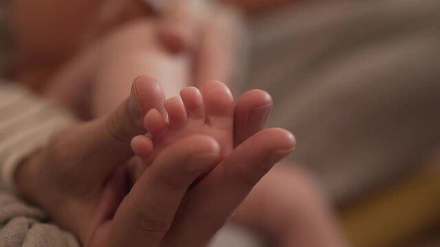 The hand of a young man holds the leg of a newborn 