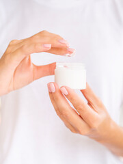 Beauty cream mockup. Close up perfect skin feminine hands apply face cream from an opened glass bottle. Vertical Front view, space for branding