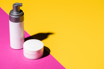 dispenser with lotion and container with cosmetic cream on pink and yellow