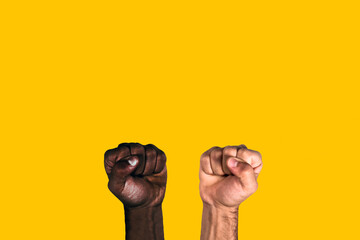 African black fist and caucasian white fist raised calling for freedom and equality on a yellow background. Multicultural fists raised.