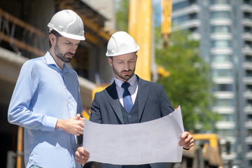 Foreman and building supervisor holding blueprint, studying it