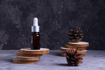 Moisturizing serum with collagen and mucin of a snail for face skin against wrinkles and acne in a glass bottle on wooden supports with cones on a gray background