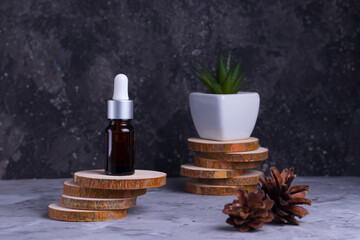 Fototapeta na wymiar Moisturizing serum with collagen and mucin of a snail for face skin against wrinkles and acne in a glass bottle on wooden supports with green succulent on a gray background