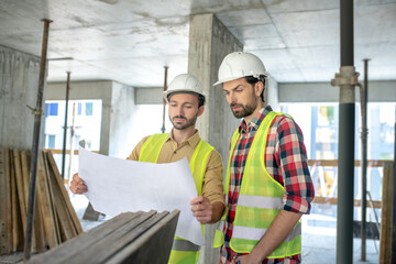 Building worker showing blueprint to his colleague, both brainstorming over it