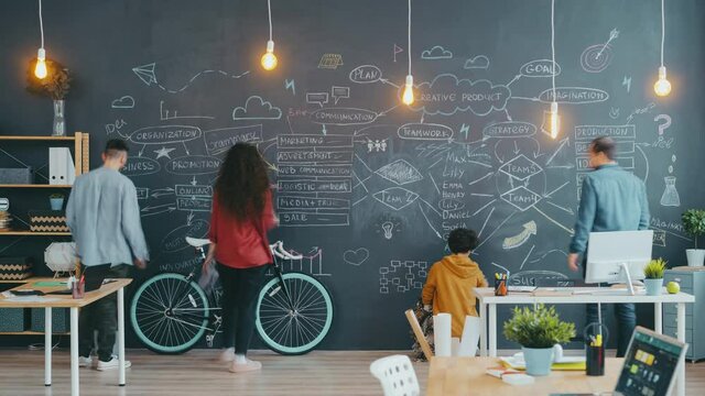Time lapse of diverse group of people writing and drawing on chalkboard wall in open space office concentrated on creative work. Workplace and business concept.