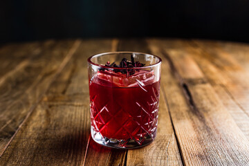 A hibiscus cocktail with an ice cube in a rocks glass on wooden table