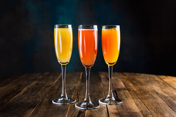 Three different sparkling fruity cocktails, red, yellow and orange, in flute glasses