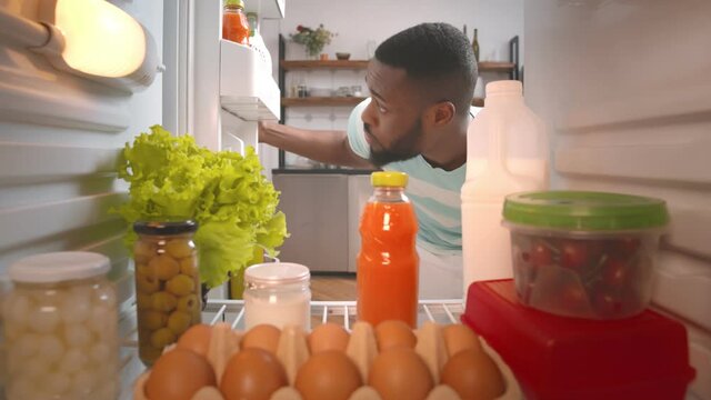 African young guy looking for meal to eat in fridge