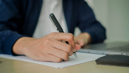 close up businessman hand using ball-point pen to writing about list of work from online webinar meeting for work from home concept
