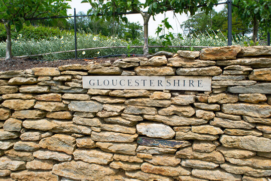 A sign of the county of Gloucestershire set into dry stone wall in a garden.