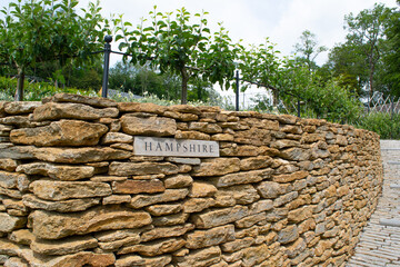 A sign of the county of Hampshire set into dry stone wall within a garden.