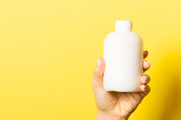 Female hand holding cosmetics bottle at yellow background with empty space for your design