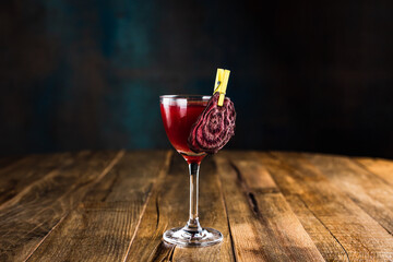 A classic red sour cocktail in a nick and nora glass garnished with a slice of beet